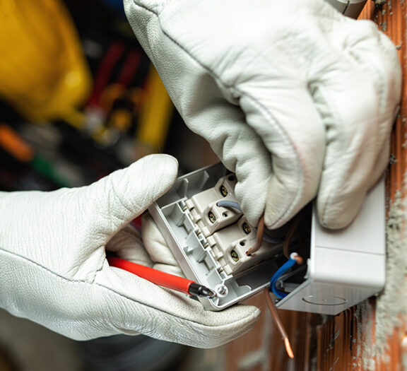 Gloved hands wiring an electrical outlet box with red and blue wires nearby