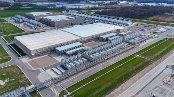 Aerial view of a large industrial complex with white-roofed buildings, cooling equipment, and extensive piping network.