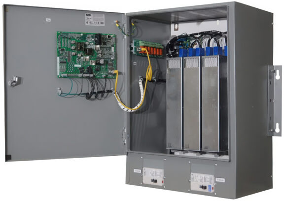 Open metal electrical cabinet showing a green circuit board on the left, bundled cables, and three tall battery modules on the right.